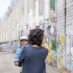 A mother and child, walk alongside the separation wall in Bethlehem, located in the West Bank. This side of the wall is a popular destination for travelers from all over the world who are drawn here to view the barrier between Israel and Palestine.